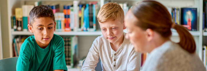 Två elever tillsammans med en lärare med bokhyllor i bakgrunden